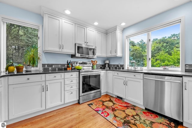 2127 E Timberlane Dr, Traverse City, MI 49686 - kitchen with a sink, dark countertops, appliances with stainless steel finishes, light wood-style floors, and white cabinetry