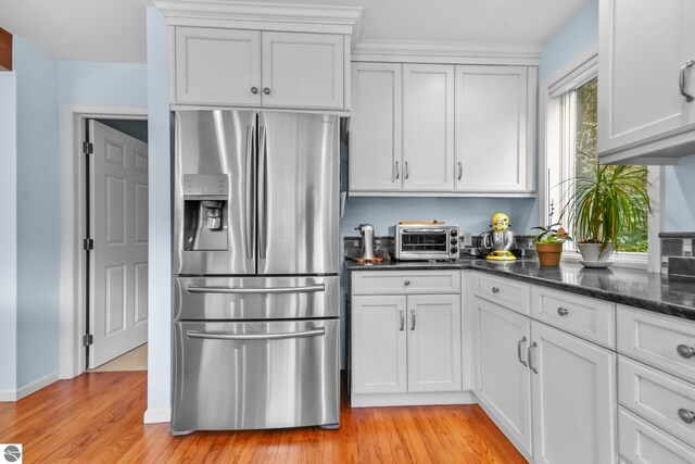 2127 E Timberlane Dr, Traverse City, MI 49686 - kitchen with white cabinets, stainless steel fridge, light wood finished floors, dark stone counters, and a toaster