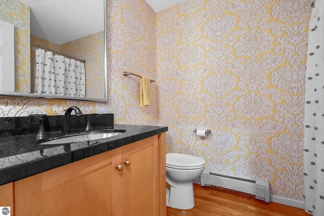 2127 E Timberlane Dr, Traverse City, MI 49686 - full bathroom with toilet, a baseboard radiator, vanity, wood finished floors, and wallpapered walls