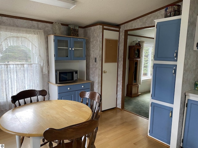 dining room featuring a textured ceiling, ornamental molding, wallpapered walls, and light wood-style floors