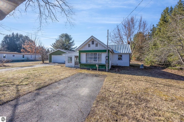 bungalow-style house featuring aphalt driveway, a standing seam roof, an outdoor structure, metal roof, and a garage