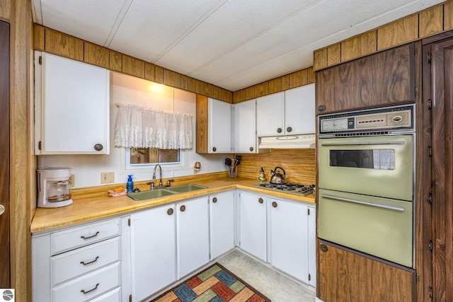 kitchen with stainless steel gas stovetop, white cabinetry, under cabinet range hood, light countertops, and a sink