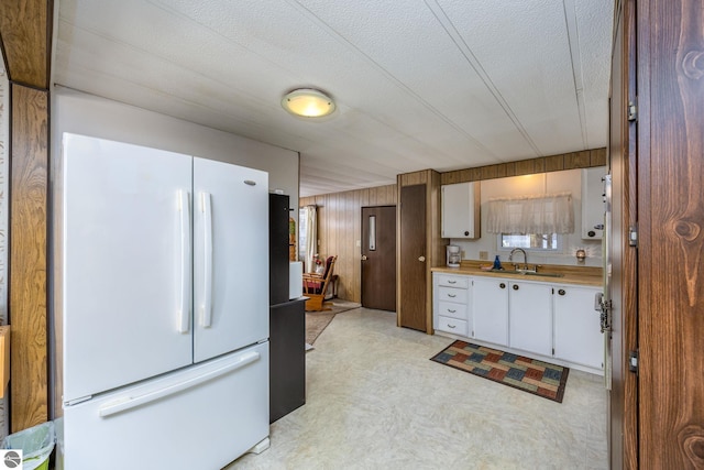 kitchen with a sink, light countertops, freestanding refrigerator, a textured ceiling, and white cabinetry