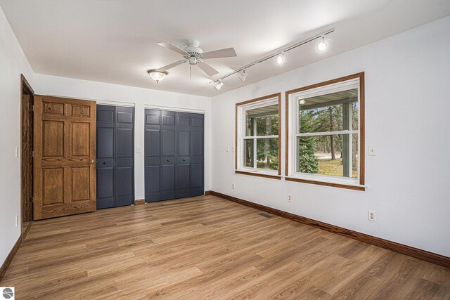 4676 W Mcmillan Rd, Muskegon, MI 49445 - unfurnished bedroom featuring baseboards, light wood-type flooring, multiple closets, and rail lighting