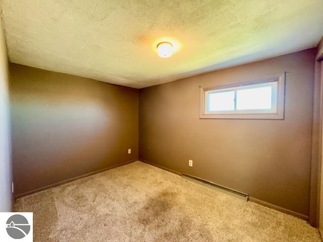 1705 S State Rd, Ithaca, MI 48847 - empty room featuring baseboards, a textured ceiling, carpet flooring, and baseboard heating