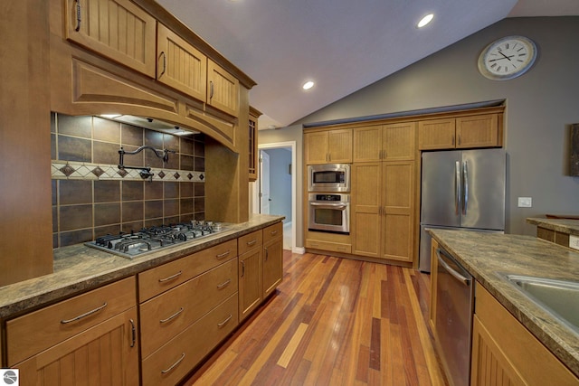 kitchen with light wood-style flooring, brown cabinetry, appliances with stainless steel finishes, lofted ceiling, and decorative backsplash