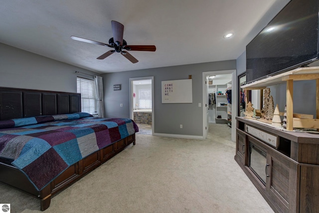 bedroom featuring ensuite bath, a ceiling fan, light carpet, a walk in closet, and baseboards