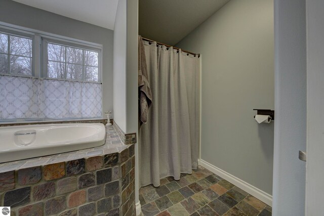 full bath featuring curtained shower, baseboards, a garden tub, and stone tile flooring