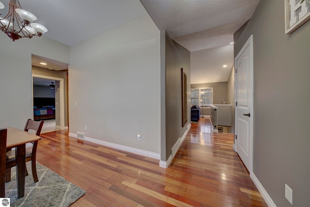 hallway with visible vents, baseboards, light wood finished floors, and a chandelier