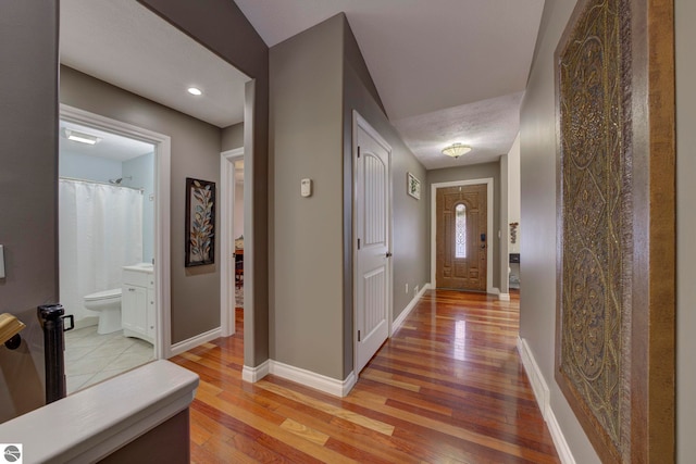 hallway with baseboards, light wood finished floors, and recessed lighting
