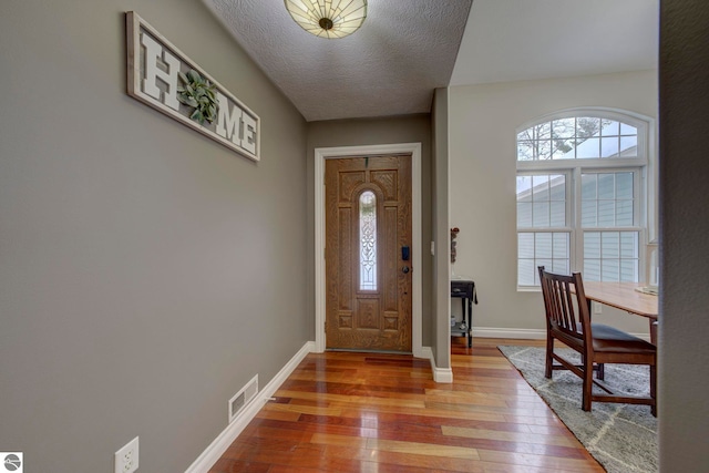 foyer with plenty of natural light, light wood-style flooring, baseboards, and a textured ceiling