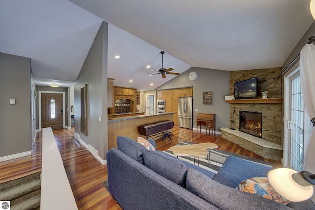 living room featuring ceiling fan, a fireplace, light wood-style flooring, vaulted ceiling, and baseboards