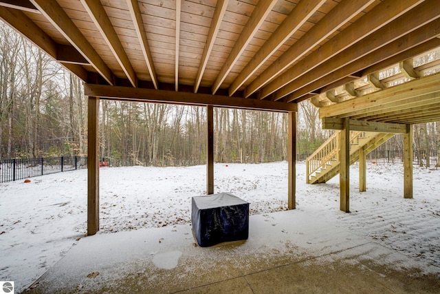 snow covered patio featuring a wooded view, fence, and stairway