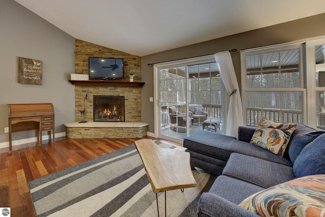 living area featuring wood finished floors, baseboards, a stone fireplace, and lofted ceiling