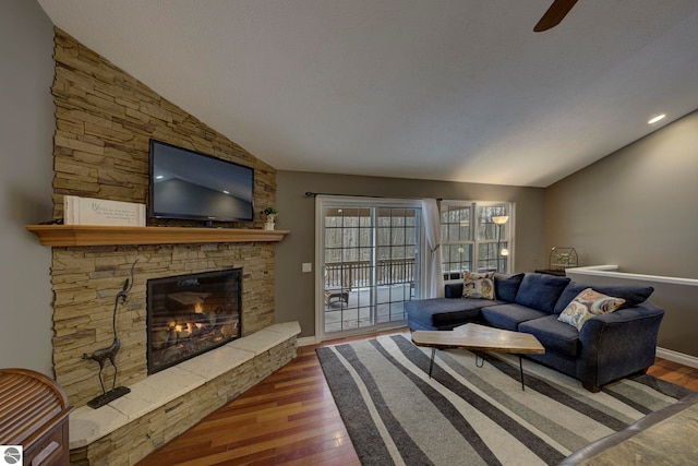 living room with wood-type flooring, a stone fireplace, a ceiling fan, and vaulted ceiling