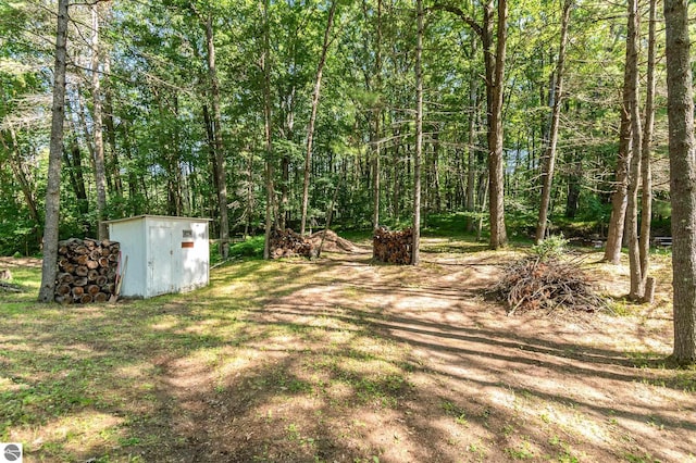view of yard with an outbuilding, a view of trees, and a storage unit