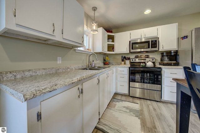 kitchen with a sink, stainless steel appliances, light wood finished floors, light countertops, and white cabinets