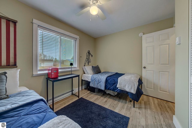 bedroom with a baseboard heating unit, baseboards, wood finished floors, and ceiling fan