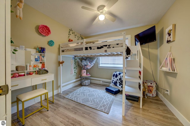 bedroom with a baseboard radiator, wood finished floors, a ceiling fan, and baseboards