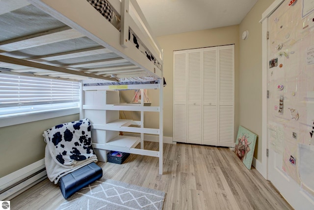 bedroom featuring a baseboard radiator, wood finished floors, a closet, and baseboards