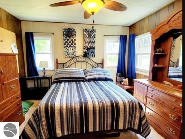 13876 Merrill Ave, Kalkaska, MI 49646 - bedroom with a ceiling fan, wood walls, and multiple windows