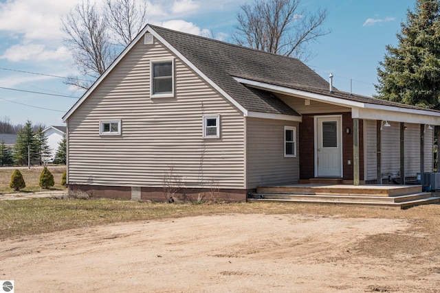 view of front of property featuring cooling unit, a shingled roof, and covered porch