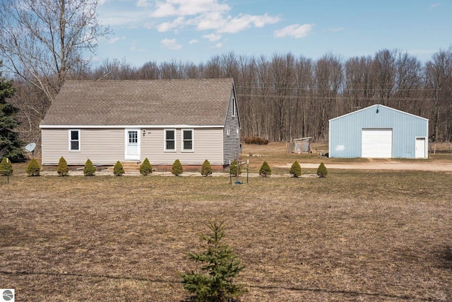 view of front facade with a garage, an outbuilding, a shingled roof, and a front yard