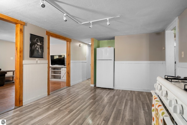 kitchen with wainscoting, track lighting, white appliances, and a textured ceiling