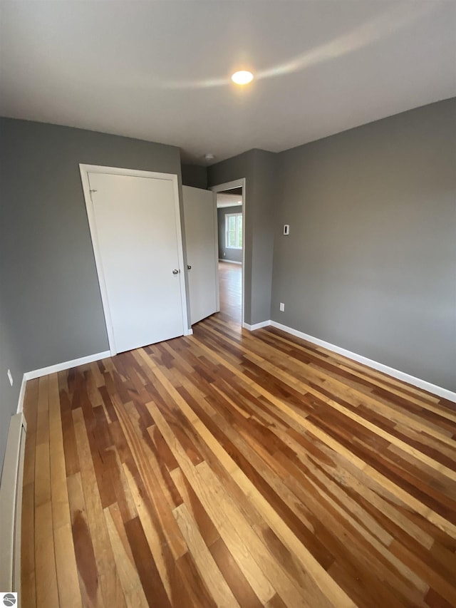 7228B S M-88, Bellaire, MI 49615 - unfurnished bedroom featuring a baseboard heating unit, hardwood / wood-style floors, and baseboards