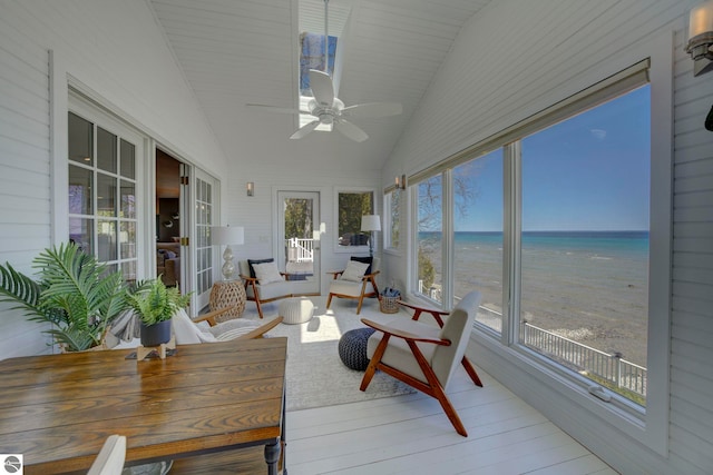 sunroom / solarium featuring a beach view, vaulted ceiling, a water view, and wood finished floors