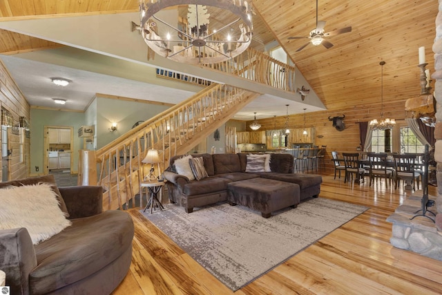 living area with high vaulted ceiling, stairs, wood finished floors, a chandelier, and wood walls