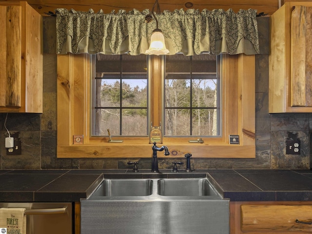 kitchen with brown cabinets, dark countertops, decorative backsplash, and a sink