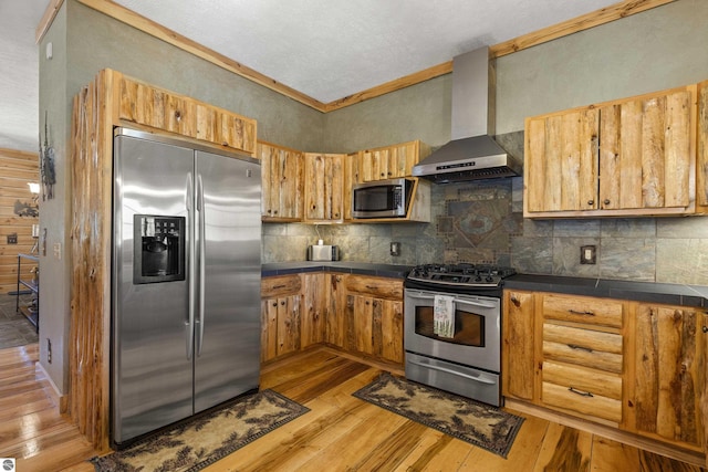 kitchen featuring stainless steel appliances, light wood-type flooring, decorative backsplash, wall chimney range hood, and tile counters