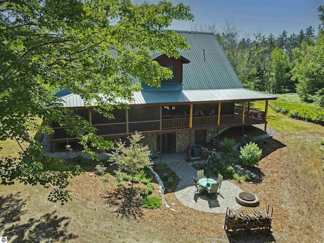back of house with a deck, a patio area, stone siding, a fire pit, and metal roof