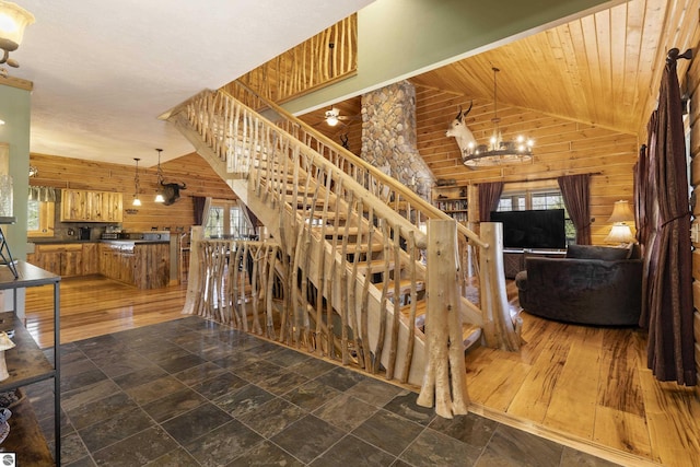 staircase with an inviting chandelier, wooden walls, stone finish floor, and high vaulted ceiling