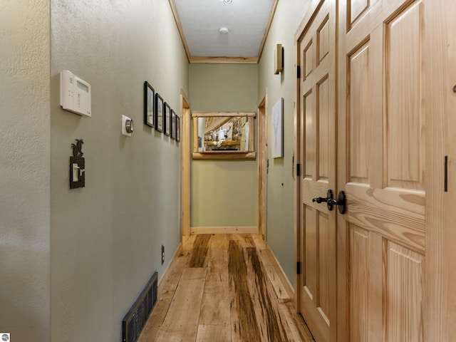 hall featuring baseboards, light wood-style floors, and visible vents