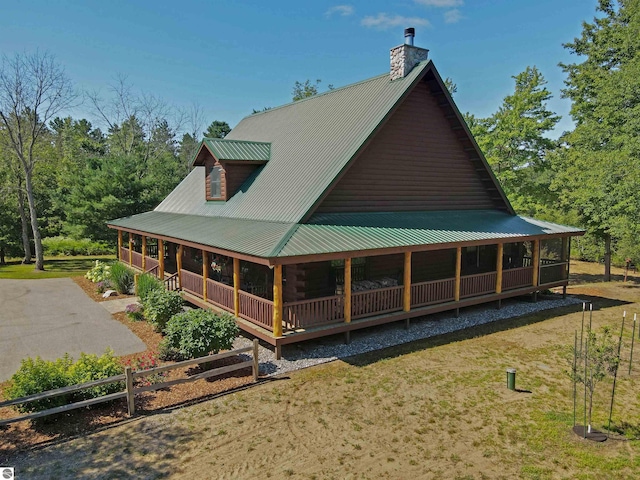 back of property with a chimney, metal roof, covered porch, fence, and a yard