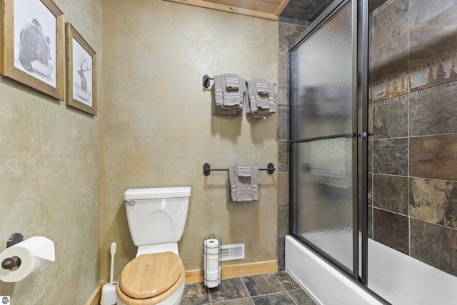 full bath featuring baseboards, enclosed tub / shower combo, toilet, stone finish floor, and visible vents