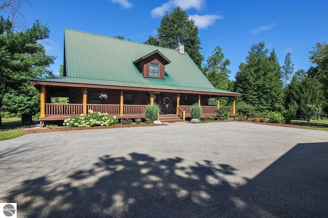 log-style house featuring a chimney, a porch, and metal roof