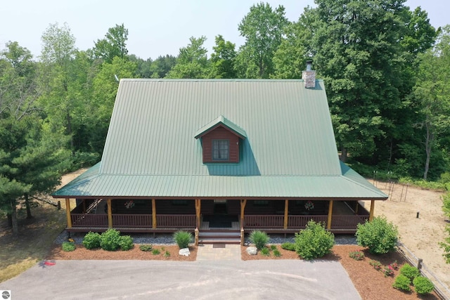 view of front of home with metal roof, a wooded view, a chimney, and covered porch