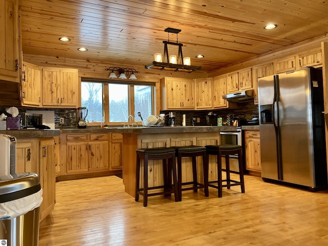kitchen featuring dark countertops, a kitchen bar, wood ceiling, under cabinet range hood, and appliances with stainless steel finishes