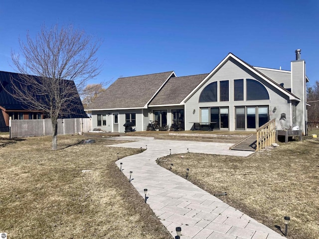 back of house featuring roof with shingles, a chimney, and fence