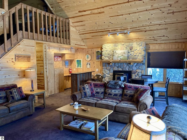 carpeted living room with vaulted ceiling, wood walls, wood ceiling, a stone fireplace, and rail lighting