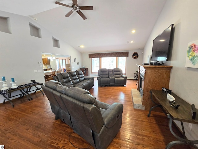 living area featuring high vaulted ceiling, a ceiling fan, wood finished floors, and a fireplace with raised hearth