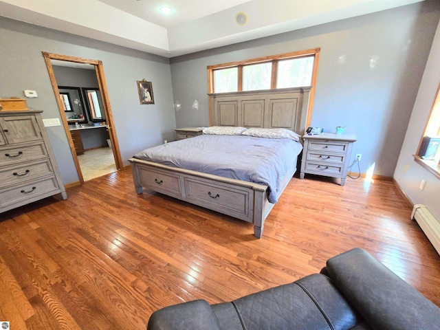 bedroom featuring a baseboard heating unit, baseboards, a raised ceiling, and light wood-type flooring