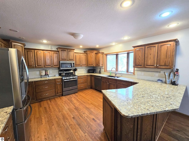 kitchen featuring stainless steel appliances, a peninsula, a sink, decorative backsplash, and wood finished floors
