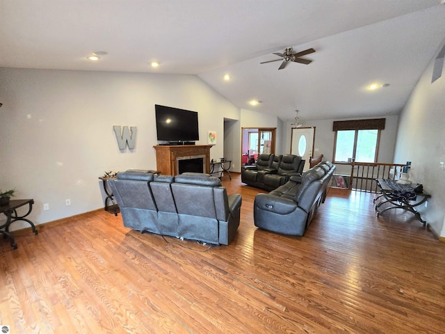 living area featuring light wood finished floors, vaulted ceiling, baseboards, ceiling fan, and a fireplace