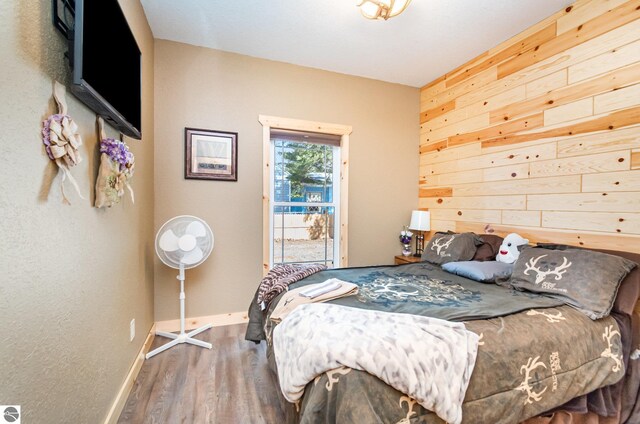3901 W Thendara Dr, Gladwin, MI 48624 - bedroom featuring baseboards, wooden walls, wood finished floors, and access to outside