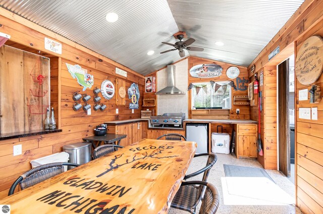 3901 W Thendara Dr, Gladwin, MI 48624 - kitchen featuring wall chimney exhaust hood, vaulted ceiling, wood walls, ceiling fan, and refrigerator