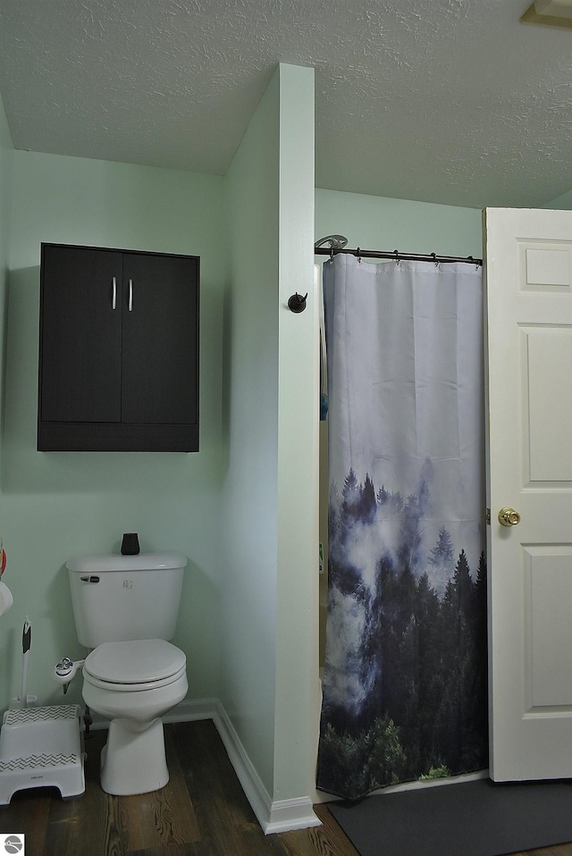 full bathroom featuring a shower with curtain, a textured ceiling, toilet, baseboards, and wood finished floors